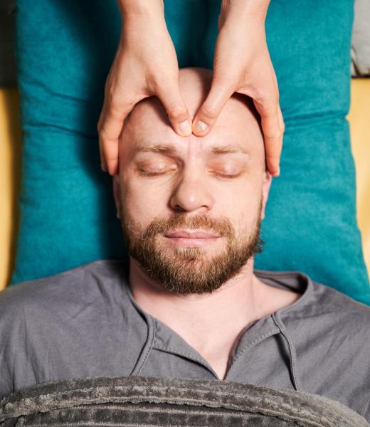 Close up of man getting thai face massage. Masseuse doing traditional massage treatment for male patient. Bald client with closed eyes, meditating, enjoying hand massage in calm atmosphere.